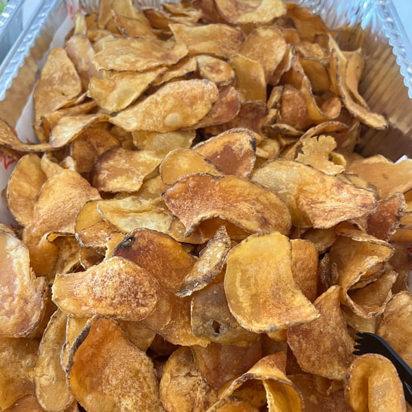 A catering tray filled with golden-brown, crispy potato chips, with a black serving tong visible.