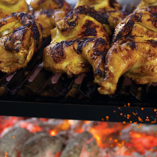 FlyBird Chargrilled Chicken cooking on a grill over glowing red coals with sparks.