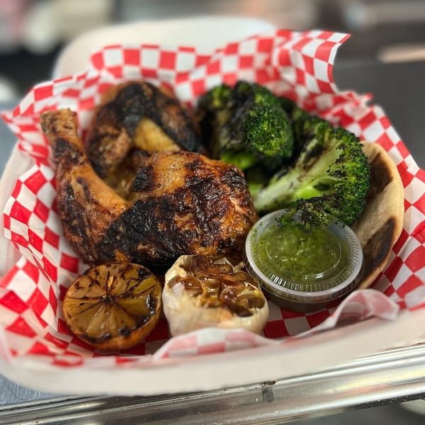 FlyBird's chargrilled chicken, broccoli, roasted garlic, grilled lemon, and green sauce in a red-checkered basket.