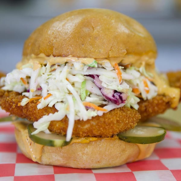 FlyBird's crispy chicken sandwich with coleslaw, pickles, and sauce on a red checkered paper.
