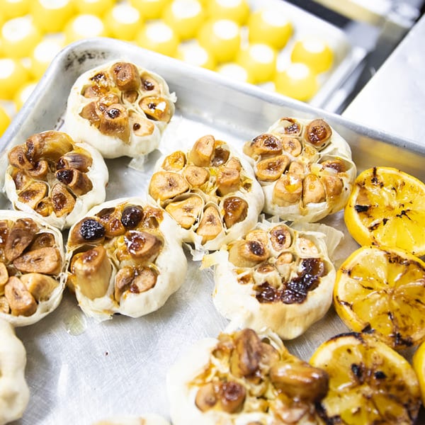 Roasted garlic bulbs and grilled lemon halves on a metal tray, ready to be served.