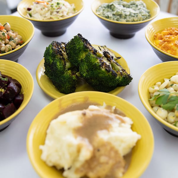 A variety of FlyBird's side dishes, including mashed potatoes, grilled broccoli, and corn, in yellow bowls.